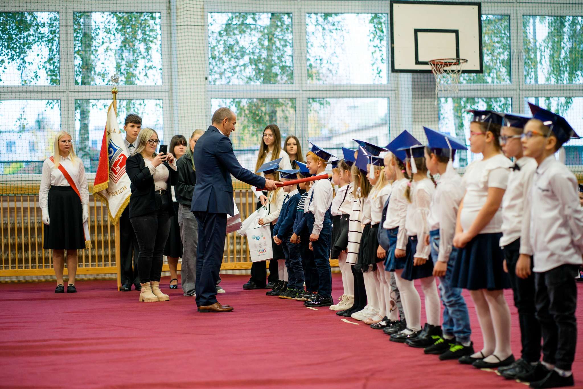 Na zdjęciu widać dyrektora szkoły wraz z uczniami w trakcie pasowania na ucznia.